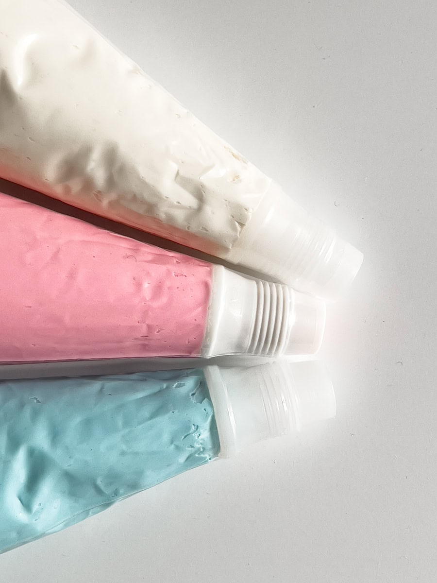 Three buttercream bags in light blue, light pink, and white. All buttercream piping bags are fitted with couplers.